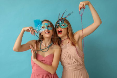 Téléchargez les photos : Belles jeunes femmes en masques de carnaval sur fond bleu - en image libre de droit