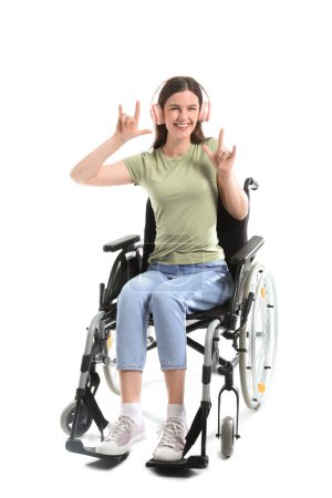 Téléchargez les photos : Jeune femme en fauteuil roulant avec écouteurs montrant "cornes du diable" sur fond blanc - en image libre de droit