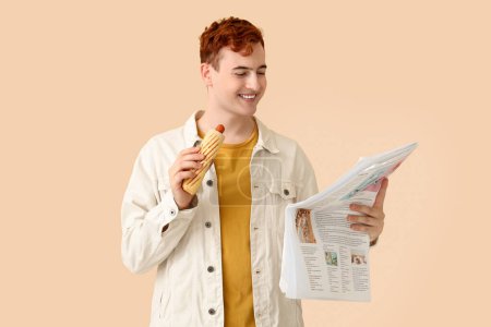 Photo for Young man with tasty hot dog and newspaper on beige background - Royalty Free Image