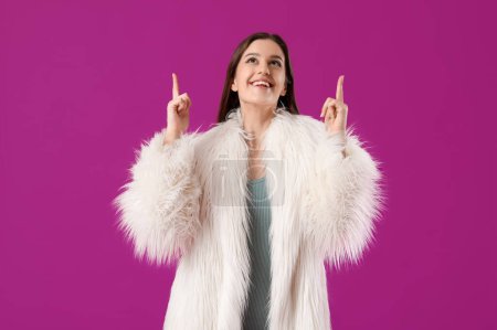 Téléchargez les photos : Jeune femme en manteau de fourrure pointant quelque chose sur fond violet - en image libre de droit