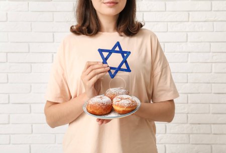 Photo for Pretty young woman with sufganiyots and David star on white brick wall background. Hanukkah celebration - Royalty Free Image