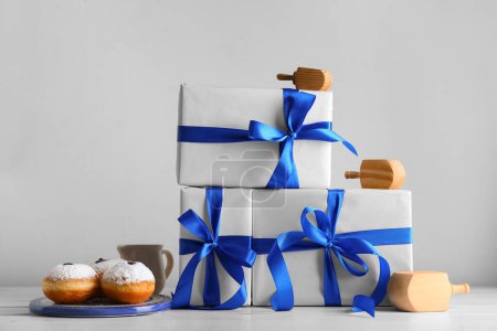 Photo for Gifts for Hanukkah celebration, tasty donuts and and dreidels on light background - Royalty Free Image