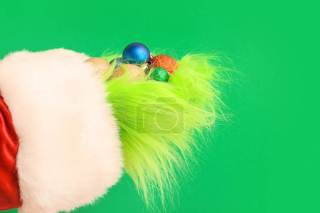 Téléchargez les photos : Mains poilues vertes de créature en costume de Père Noël avec des boules de Noël sur fond vert - en image libre de droit