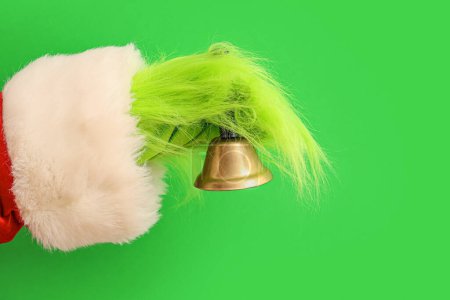 Photo for Green hairy hand of creature in Santa costume with Christmas bell on green background - Royalty Free Image
