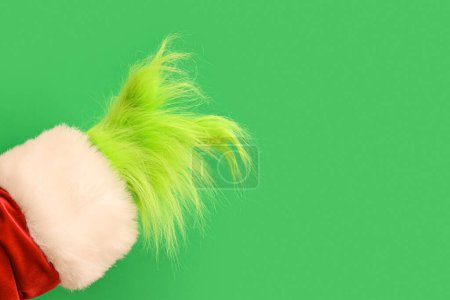 Téléchargez les photos : Main poilue verte de créature en costume de Père Noël pointant quelque chose sur fond vert - en image libre de droit
