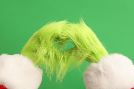 Photo for Green hairy hands of creature in Santa costume showing heart gesture on green background - Royalty Free Image