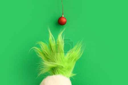 Téléchargez les photos : Main poilue verte de créature en costume de Père Noël avec boule de Noël sur fond vert - en image libre de droit
