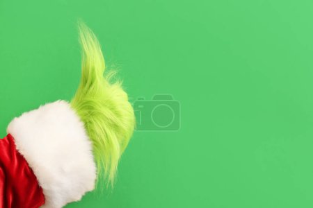 Photo for Green hairy hand of creature in Santa costume showing thumb-up gesture on green background - Royalty Free Image