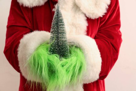 Foto de Verde manos peludas de la criatura en traje de Santa con abeto decorativo sobre fondo blanco, primer plano - Imagen libre de derechos