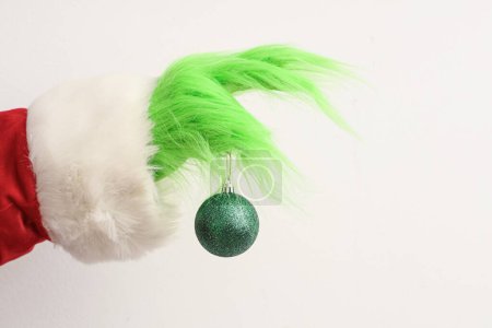 Téléchargez les photos : Main poilue verte de créature en costume de Père Noël avec boule de Noël sur fond blanc - en image libre de droit