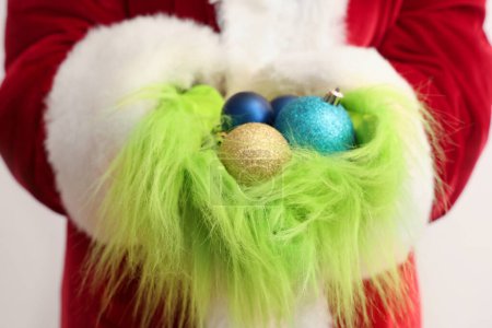 Foto de Verde manos peludas de criatura en traje de Santa con bolas de Navidad sobre fondo blanco, primer plano - Imagen libre de derechos
