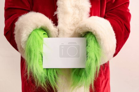 Téléchargez les photos : Mains poilues vertes de créature en costume de Père Noël avec carte blanche sur fond blanc, gros plan - en image libre de droit