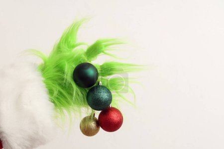 Photo for Green hairy hand of creature in Santa costume with Christmas balls on white background - Royalty Free Image