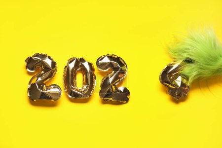 Photo for Green hairy hand of creature in Santa costume with figure 2024 made of balloons on yellow background - Royalty Free Image