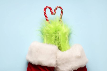 Photo for Green hairy hands of creature in Santa costume with candy canes on blue background - Royalty Free Image