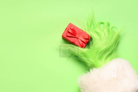 Foto de Mano peluda verde de la criatura en traje de Santa con caja de regalo de Navidad sobre fondo verde - Imagen libre de derechos