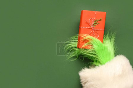 Téléchargez les photos : Main poilue verte de créature en costume de Père Noël avec boîte cadeau de Noël sur fond vert - en image libre de droit