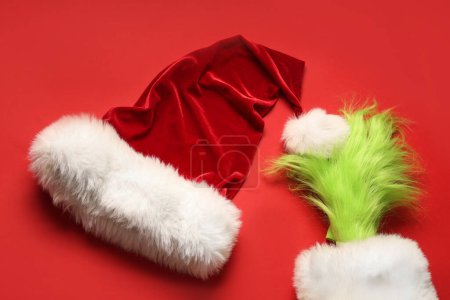 Photo for Green hairy hand of creature with Santa hat on red background - Royalty Free Image
