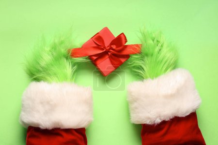 Photo for Green hairy hands of creature in Santa costume with Christmas gift box on green background - Royalty Free Image