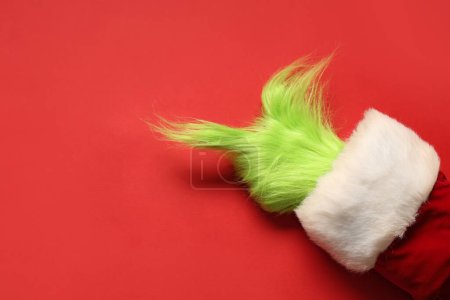 Téléchargez les photos : Main poilue verte de créature en costume de Père Noël pointant quelque chose sur fond rouge - en image libre de droit