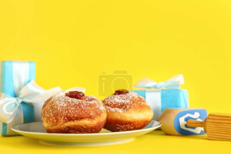 Photo for Dreidels with gift boxes and tasty donuts on yellow background. Hanukkah celebration - Royalty Free Image