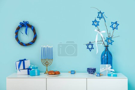 Téléchargez les photos : Armoire blanche avec menorah, dreidels, sufganiyots et coffrets cadeaux près du mur bleu. Hanoukka célébration - en image libre de droit