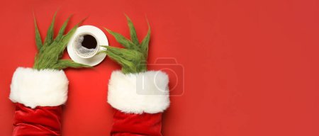 Photo for Green hairy hands of creature in Santa costume and cup of coffee on red background with space for text - Royalty Free Image