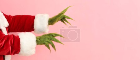Grüne haarige Hände der Kreatur im Weihnachtsmannkostüm auf rosa Hintergrund mit Platz für Text 