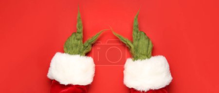 Téléchargez les photos : Mains poilues vertes de créature en costume de Père Noël pointant quelque chose sur fond rouge - en image libre de droit