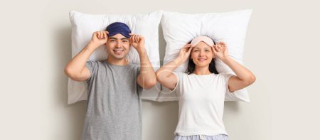 Téléchargez les photos : Jeune couple avec des masques de couchage et des oreillers sur fond clair - en image libre de droit