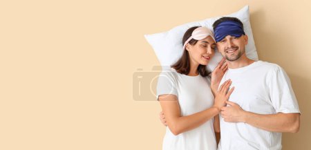 Photo for Young couple with sleeping masks and pillow on beige background with space for text - Royalty Free Image