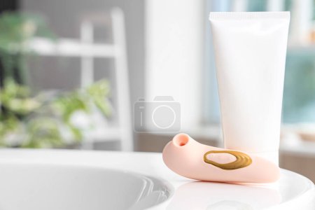 Photo for Vibrator with tube of cream on bathtub in room, closeup - Royalty Free Image