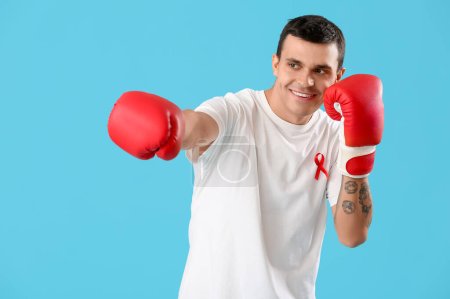 Photo for Young man with red ribbon and boxing gloves on blue background. World AIDS day concept - Royalty Free Image