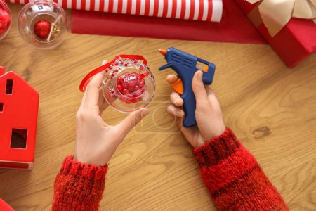 Téléchargez les photos : Femme tenant pistolet à colle et décoration boule de Noël avec strass sur la table - en image libre de droit