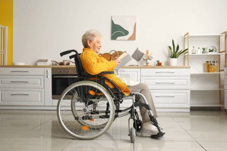 Téléchargez les photos : Femme âgée en fauteuil roulant livre de lecture à la maison - en image libre de droit