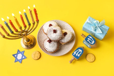 Photo for Menorah, dreidels, plate with donuts and gift box for Hanukkah celebration on blue background - Royalty Free Image