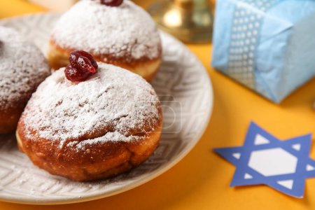 Photo for Plate with donuts and gift box for Hanukkah celebration on yellow background - Royalty Free Image