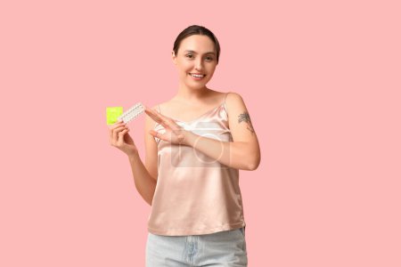Téléchargez les photos : Belle jeune femme avec préservatif et pilules contraceptives sur fond rose. Concept de sexe sûr - en image libre de droit