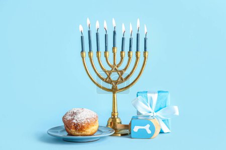 Photo for Menorah with dreidel, tasty donut and gift box on blue background. Hanukkah celebration - Royalty Free Image