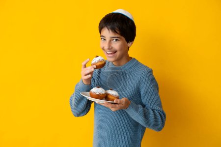 Photo for Little boy in kipa holding plate with tasty donuts on yellow background. Hanukkah celebration - Royalty Free Image