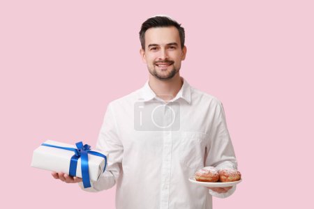 Téléchargez les photos : Beau homme adulte avec sufganiyots et coffret cadeau sur fond rose. Hanoukka célébration - en image libre de droit