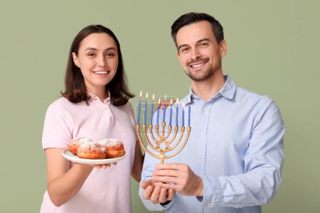 Photo for Lovely couple with menorah and sufganiyots on green background. Hanukkah celebration - Royalty Free Image