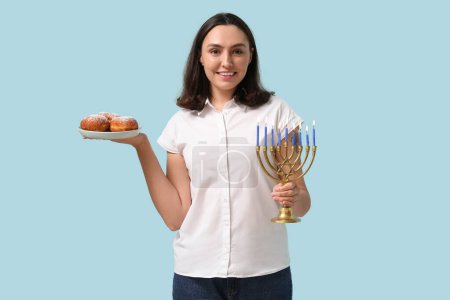 Photo for Pretty young woman with menorah and sufganiyots on blue background. Hanukkah celebration - Royalty Free Image