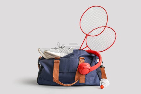 Photo for Sports bag with sneakers, headphones, badminton rackets and shuttlecock on grey background - Royalty Free Image