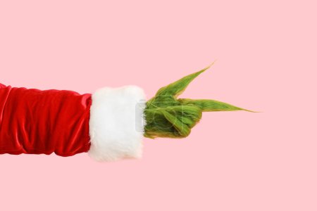 Photo for Green hairy hand of creature in Santa costume pointing at something on pink background - Royalty Free Image