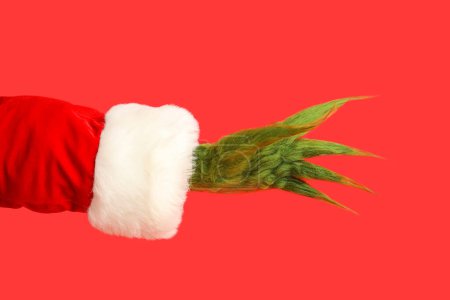 Photo for Green hairy hand of creature in Santa costume on red background - Royalty Free Image