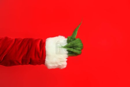 Photo for Green hairy hand of creature in Santa costume showing thumb-up gesture on red background - Royalty Free Image