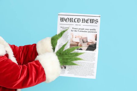 Photo for Green hairy hands of creature in Santa costume with newspaper on red background - Royalty Free Image