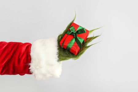 Téléchargez les photos : Main poilue verte de créature en costume de Père Noël avec boîte cadeau sur fond gris - en image libre de droit