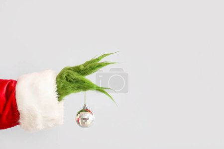 Photo for Green hairy hand of creature in Santa costume with Christmas ball on grey background - Royalty Free Image